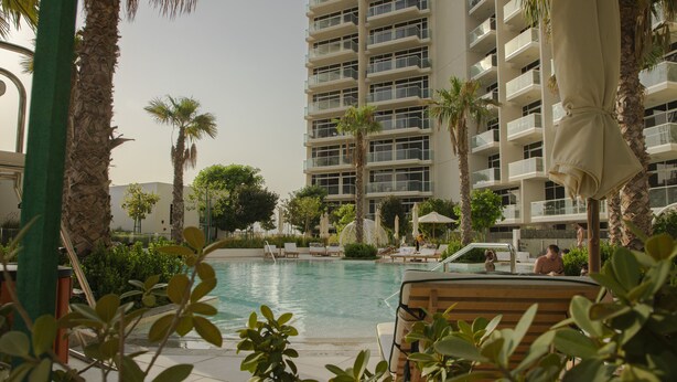 Un hotel con piscina circondata da palme e lettini.