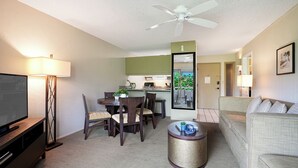A living room with a TV, sofa, and dining area with chairs and a table. - Plantation Hale K10 | 1BR Condo w/ AC, Resort pool,  Private Lanai (Kapaa)