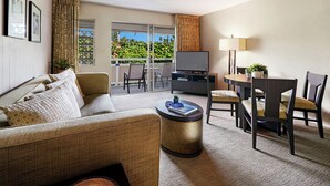 A hotel room with a sofa, a dining table with chairs, a television, and a balcony with a view of greenery. - Plantation Hale K10 | 1BR Condo w/ AC, Resort pool,  Private Lanai (Kapaa)