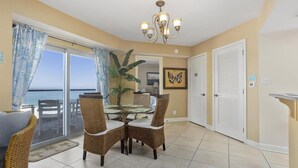 A dining area with wicker chairs and a glass table, a chandelier, and a view of the ocean through large sliding doors. - 1 Bedroom, 1 Bath Gulf Front Condo t Regency Towers 603 East! (Pensacola Beach)