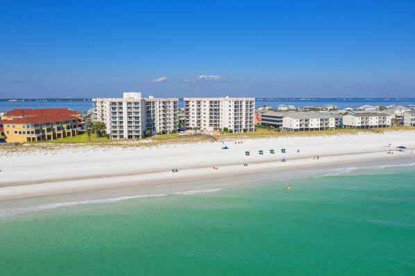 Un hotel frente a la playa con varias edificaciones, una playa de arena y aguas turquesas cristalinas.