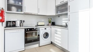 Eine moderne Küche mit weißen Schränken, einer Mikrowelle, einem Toaster, einem Backofen und einer Waschmaschine.