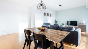 Ein modernes Wohnzimmer mit einem Holzespeisetisch, schwarzen Stühlen, einem grauen Sofa und einem Fernseher.