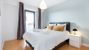 Ein modernes Schlafzimmer mit einem großen Bett, einem Nachttisch, einer Lampe und Blick ins Freie.