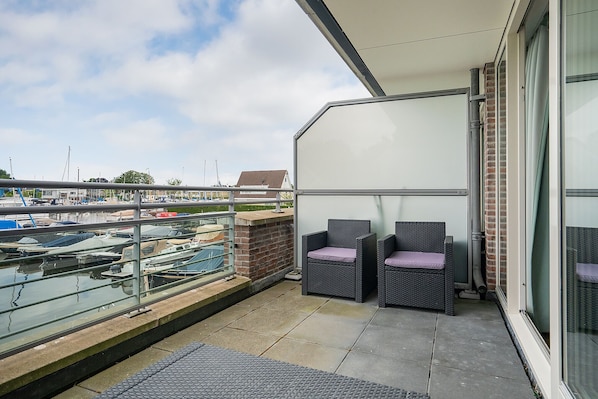 A balcony with two wicker chairs, a view of a marina with boats, and a brick wall.
