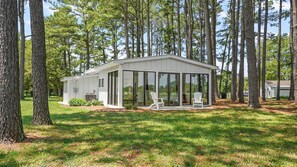 Een modern, gelijkvloers huis met een glazen patio, omgeven door hoge dennenbomen.