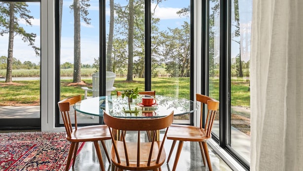 Un coin repas avec une table en verre et des chaises en bois, une tasse rouge et un vase avec une plante.