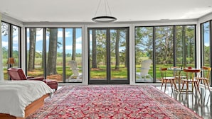 Une chambre à coucher avec un grand lit, un tapis rouge à motifs et une vue sur un jardin, visible à travers de grandes portes-fenêtres coulissantes.