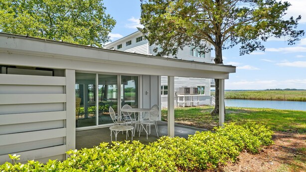 Ein modernes Haus mit überdachter Terrasse, einem Essbereich mit Gartenmöbeln und Seeblick.