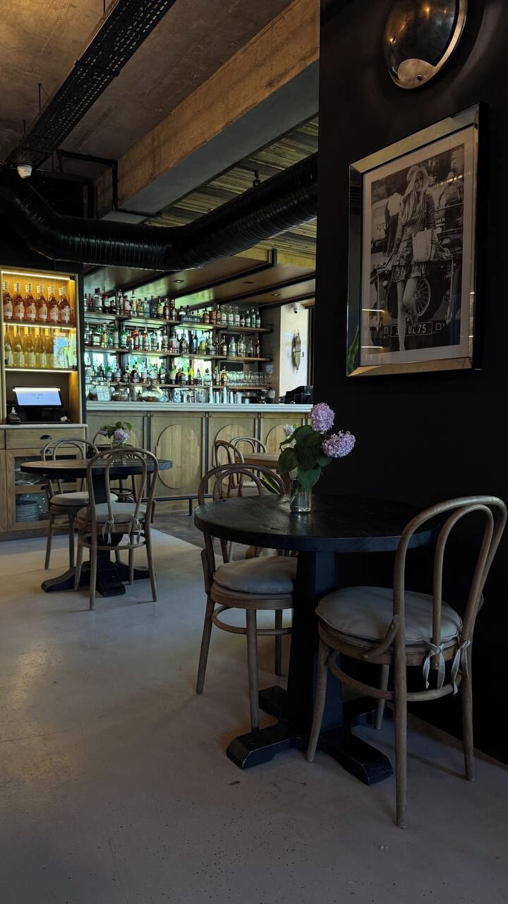 A bar area with wooden chairs, a bar counter stocked with bottles, and a vintage poster on the wall.