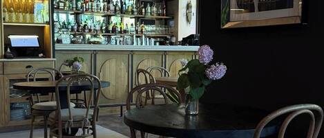 A bar area with wooden chairs, a bar counter stocked with bottles, and a vintage poster on the wall.