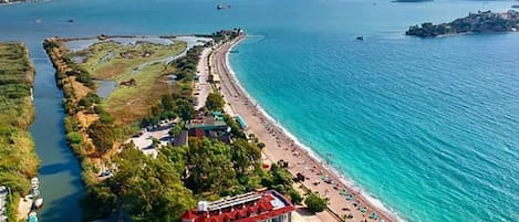 An aerial view of a coastal hotel with a beachfront, a swimming pool, and a road running parallel to the beach.