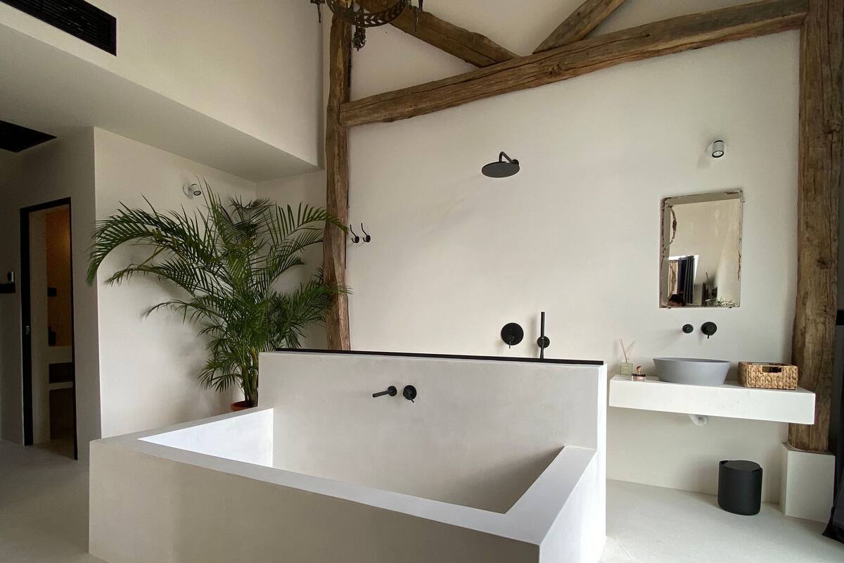 A modern bathroom with a large bathtub, a wooden ceiling, a potted plant, and a vanity with a mirror.