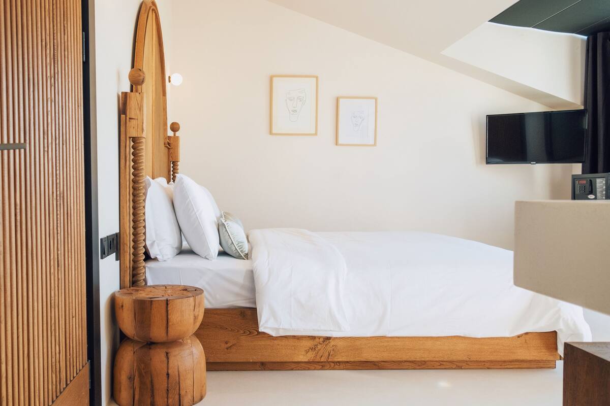 A modern bedroom with a wooden bed frame, white bedding, and a flat-screen TV on the wall.