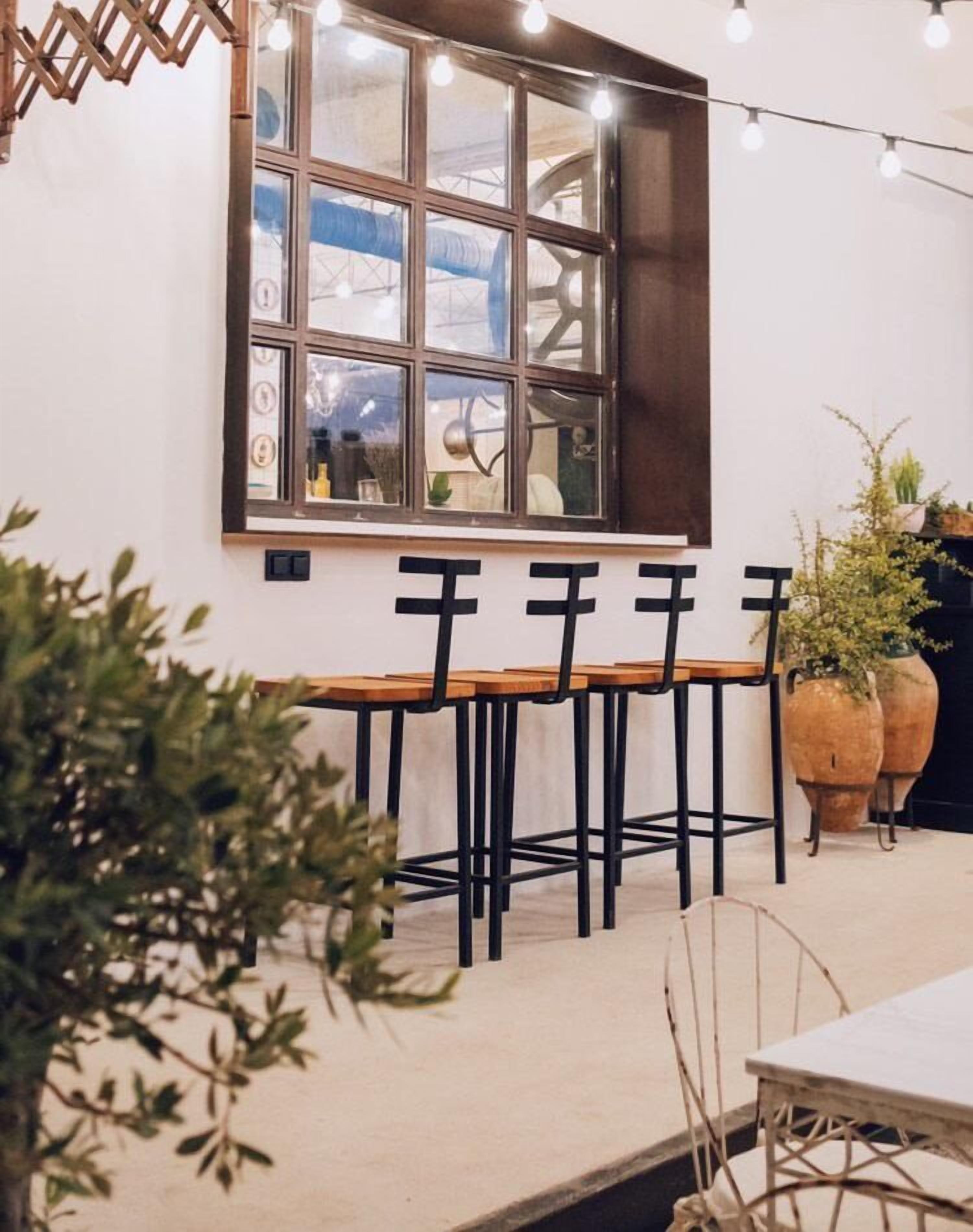 Un comedor con una mesa de madera larga y sillas negras, una ventana con varios paneles y luces colgantes.