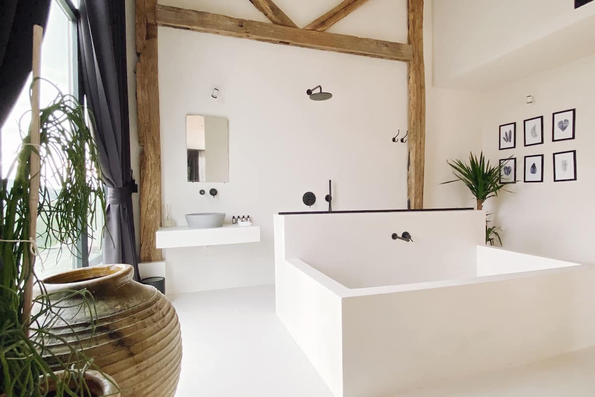 A modern bathroom with a large bathtub, a sink, and a mirror. There are potted plants and framed pictures on the walls.