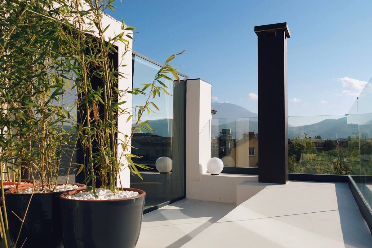 A modern balcony with potted plants, a glass railing, and a view of distant mountains.