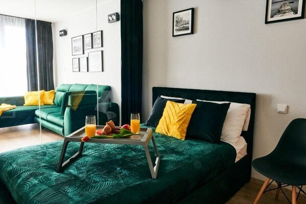 A hotel room with a bed, a chair, and a breakfast tray with fruits and juice.