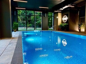 An indoor swimming pool with clear glass walls, potted plants, and a logo on the wall.