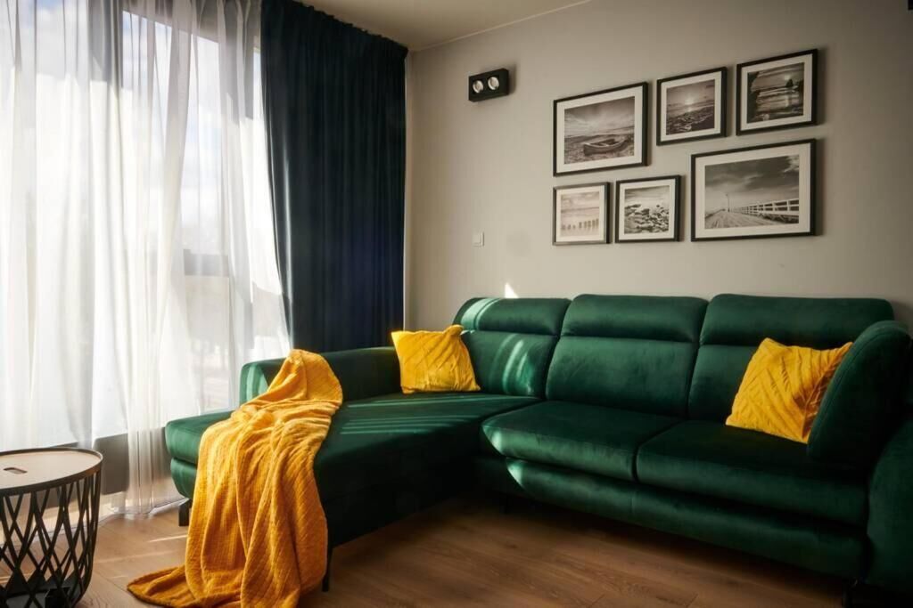 A green sofa with yellow cushions, a yellow throw blanket, and a small round table with a black base.