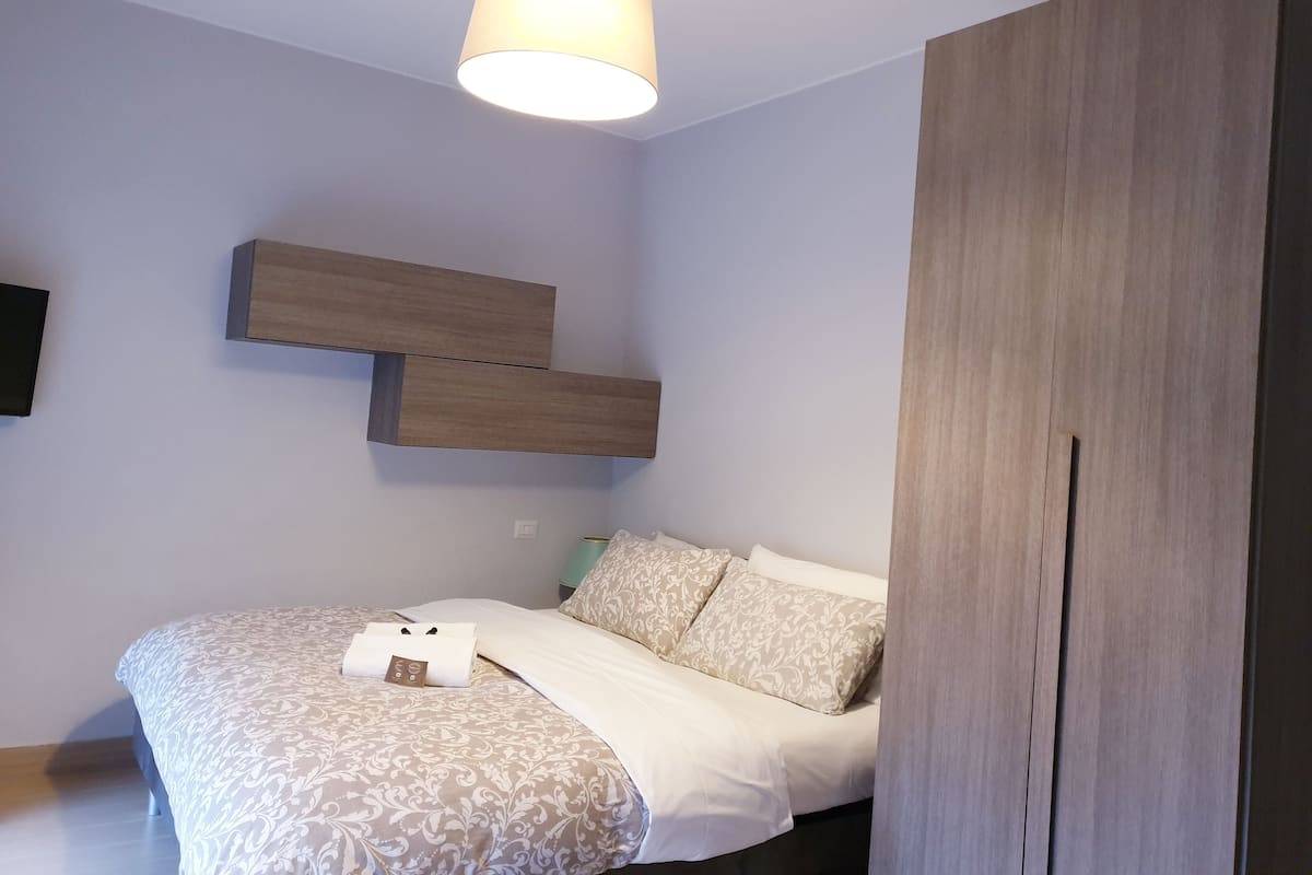 A bedroom with a bed, a hanging light fixture, and a wooden wardrobe.