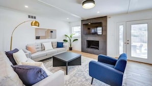 A modern living room with a sofa, armchairs, a coffee table, a fireplace, and a large window.