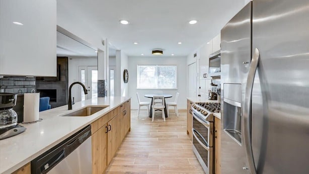 A modern kitchen with a stainless steel refrigerator, wooden cabinets, a dishwasher, and a gas stove.