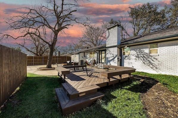 A backyard with a wooden deck, a hammock, and a brick house.