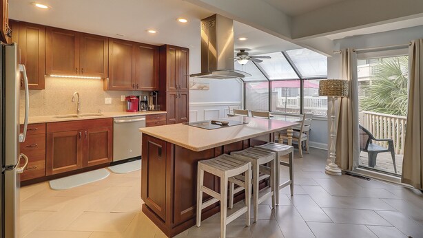 Una cocina moderna con armarios de madera, una isla central con taburetes y una zona de comedor con mesa y sillas de vidrio.