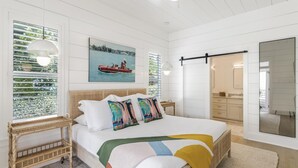 A bedroom with a bed, a window with blinds, a painting, a bedside table, and a mirror. - Bikes | Pool | Ping Pong | Beach Service (Santa Rosa Beach)
