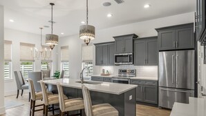 Une cuisine moderne avec des meubles gris, des appareils en acier inoxydable et un îlot central doté de chaises.