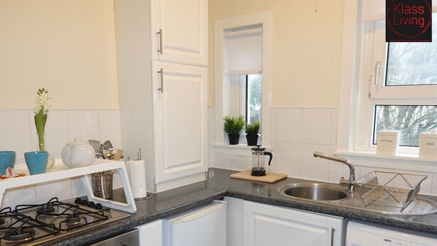 A compact kitchen with white cabinets, a gas stove, a built-in oven, a dishwasher, and a window with a view of trees.