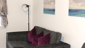 A grey sofa with purple cushions in a room with white walls and a painting of a beach.