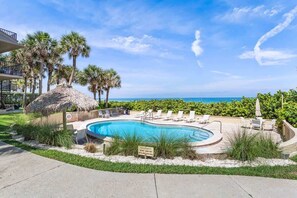 A swimming pool with lounge chairs, palm trees, and a view of the ocean. - La Concha 2 - Beachfront condo w pool (Belleair Beach)