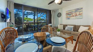 A dining area with a glass table, wooden chairs, and a view of the outdoors through large windows. - Maui Vista 2213 Kihei condo across Charley Young Beach, summer deal (Kihei)