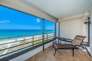 Un balcón con vista a la playa, una silla y una ventana con persianas.