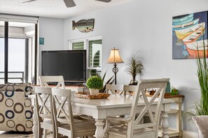 Un coin repas comprenant une table, des chaises, un téléviseur, une lampe et une décoration murale représentant des poissons.