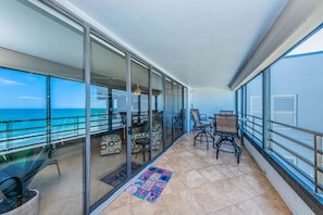Un balcón con vista al océano, puertas de vidrio y mobiliario exterior.
