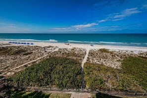 Une plage avec un ciel dégagé, un rivage sablonneux et une zone délimitée par une clôture, où l’on trouve de la végétation.
