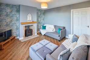 A living room with a fireplace, grey sofas, a television, and a wooden floor.