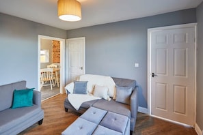 A living room with a grey sofa, a grey ottoman, and a white door.