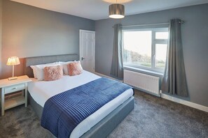 A bedroom with a bed, a nightstand, a lamp, a window with curtains, and a radiator. - Host & Stay | Woods Yard (Skelton-in-Cleveland)