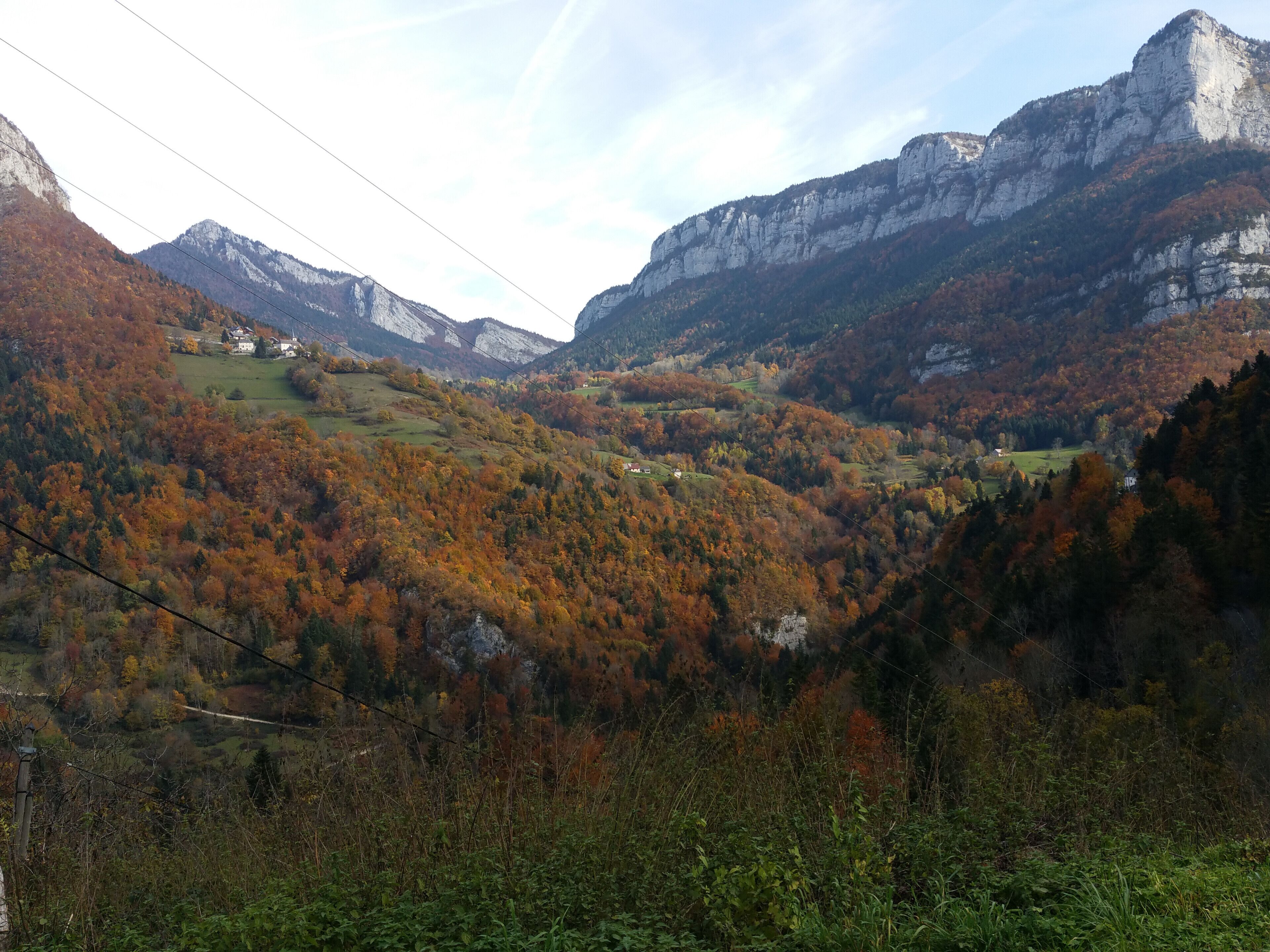 Un paysage montagneux aux couleurs automnales, avec une vallée et quelques bâtiments.