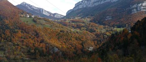 Un paysage montagneux aux couleurs automnales, avec une vallée et quelques bâtiments.