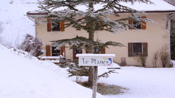 A snow-covered house with a sign reading "Le Planey" in front.