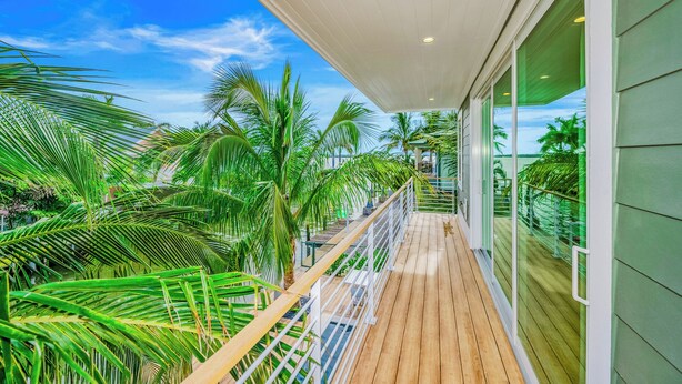 Una terraza de madera con barandilla de vidrio que da a un jardín tropical con palmeras.