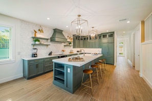 A modern kitchen with a central island, bar stools, and a large window.