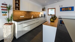 Una cocina moderna con armarios blancos, encimera de madera y horno integrado. Hay frascos decorativos en la encimera y una planta en maceta a la izquierda.