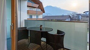 Un balcón con muebles de mimbre, una mesa de vidrio y vistas a las montañas.