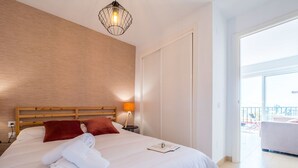 Habitación de hotel con una cama grande, cabecero de madera, una lámpara de noche y vistas al balcón exterior.